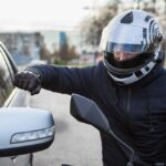 Angry motorcyclist punching car window
